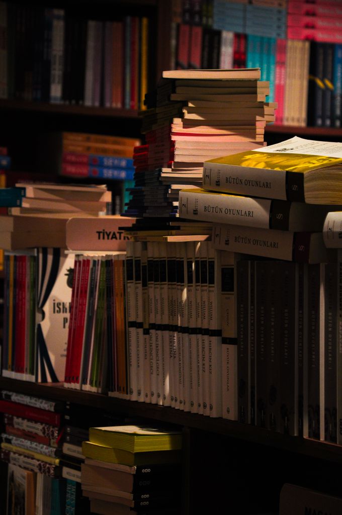 Dimly lit library scene featuring a variety of stacked books on a shelf.