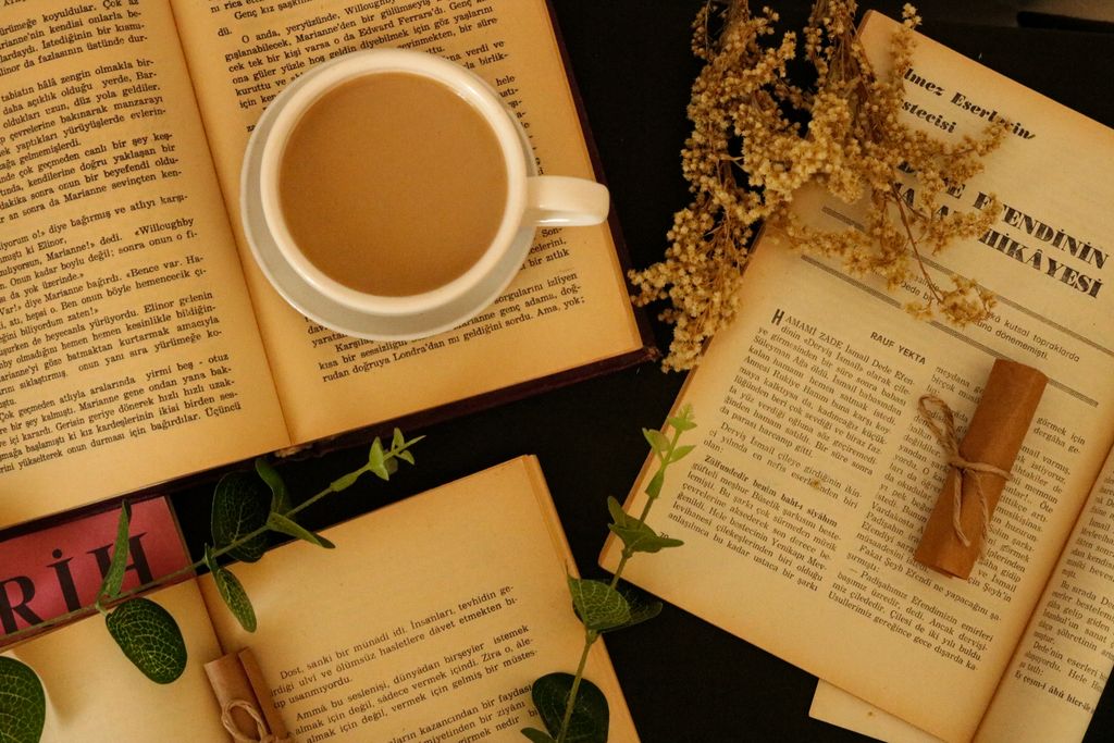 Flat lay of a coffee cup with open books and dried flowers for a cozy reading ambiance.