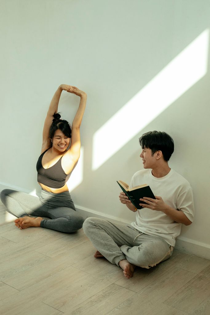 Full body of positive Asian couple in activewear sitting on floor with crossed legs while smiling and looking at each other